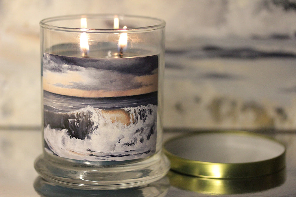 Close up of a lit sea salt scented candle with original coastal artwork on the glass jar. 