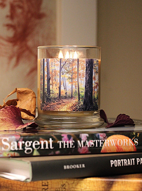 A double wicked leaves scented 9 oz. candle with original decorative artwork on the glass jar in an aesthetic  environment