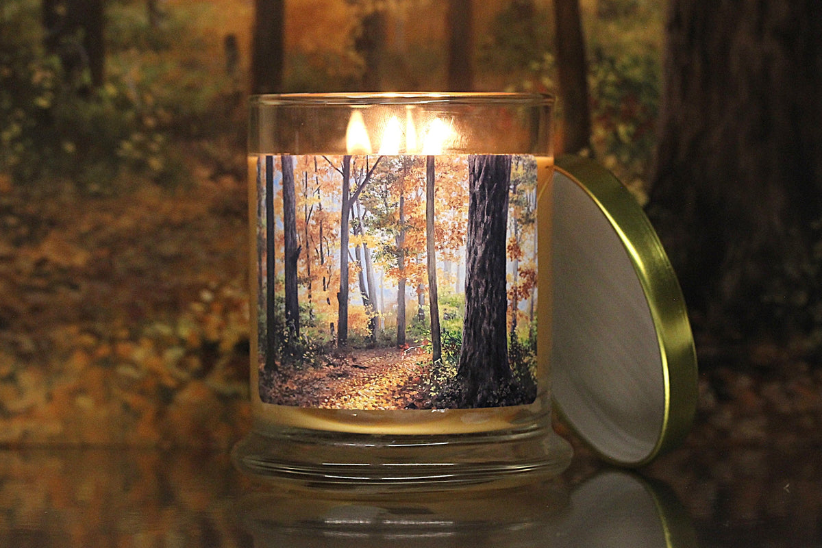 Close up view of a lit, leaves scented candle with original decorative artwork on the glass jar.