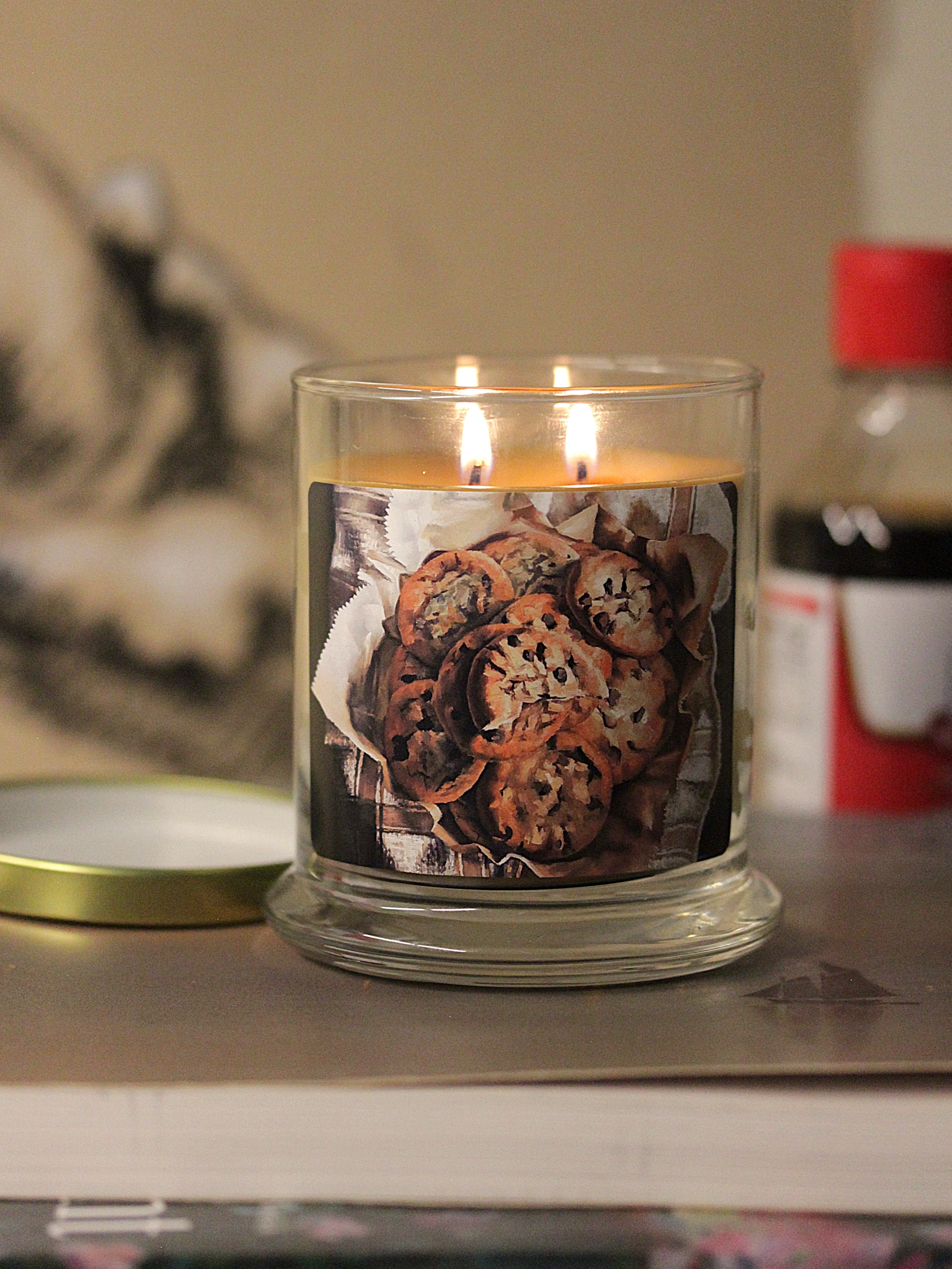 A lit 9oz vanilla scented candle with original decorative artwork on the glass jar in an aesthetic environment.