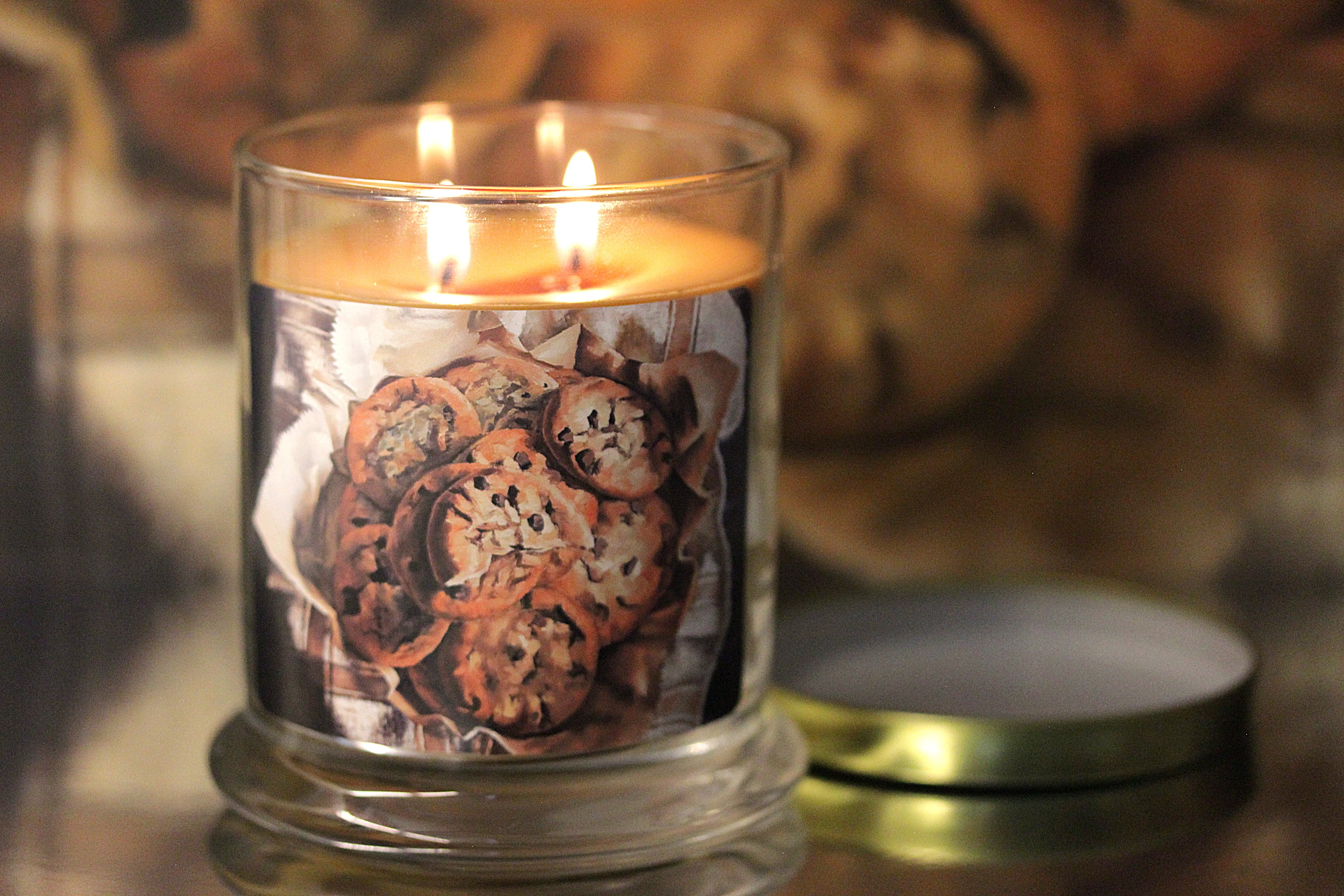 Close up view of a lit vanilla scented candle with original decorative artwork on the glass jar.