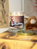 A lit 9oz cashmere scented candle with original cozy artwork on the glass jar in an aesthetic environment.