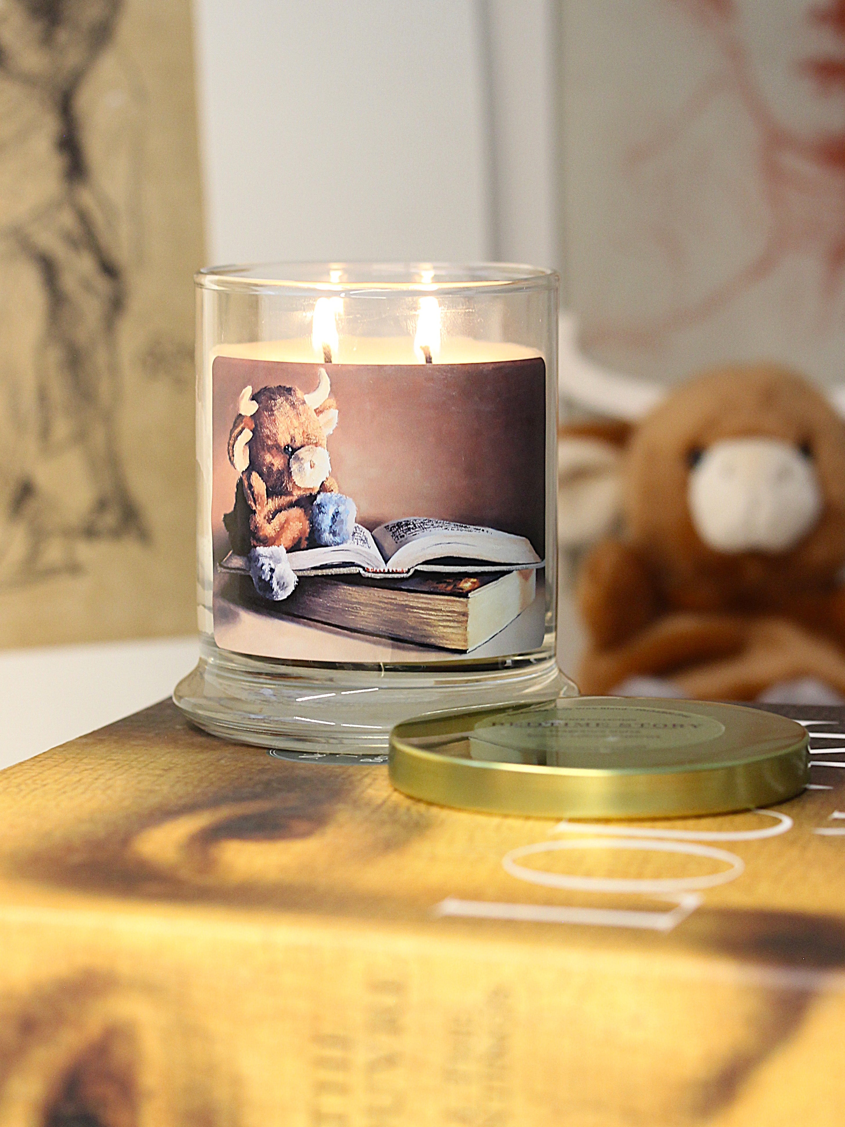 A lit 9oz cashmere scented candle with original cozy artwork on the glass jar in an aesthetic environment.