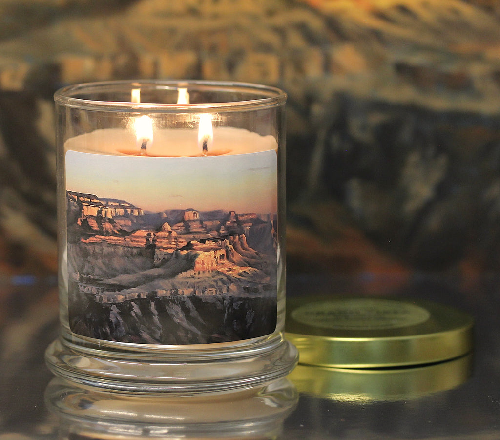 Close up view of a lit patchouli scented candle with original landscape artwork on the glass jar.