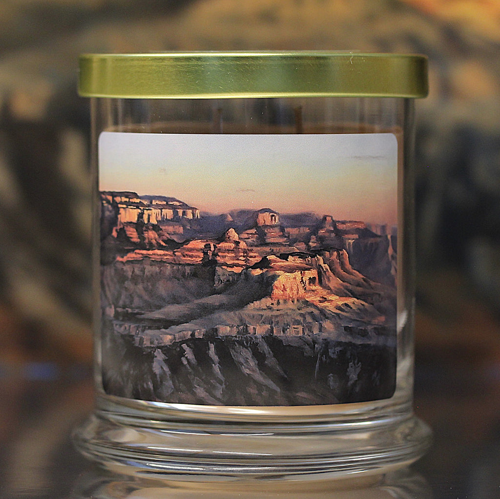 Close up view of an unlit patchouli scented candle with original landscape artwork on the glass jar.