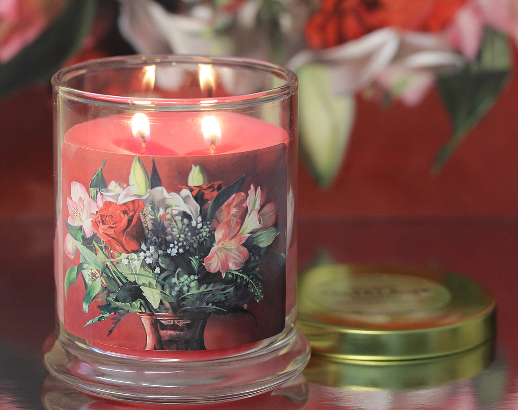 close up view of a lit rose vanilla scented candle with original floral artwork on the glass jar.
