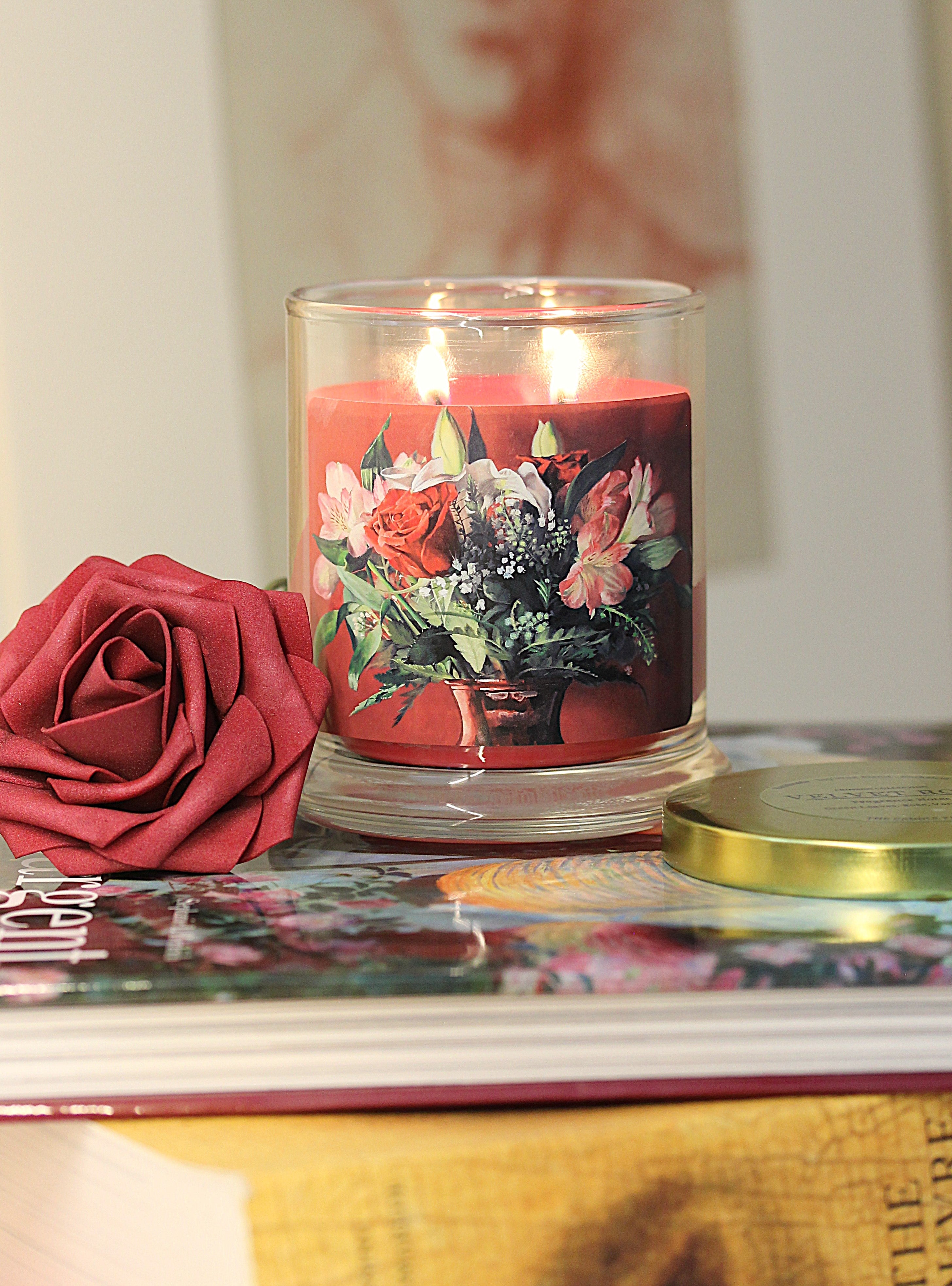 a lit 9oz rose vanilla scented candle with original floral artwork on the glass jar in an aesthetic environment.