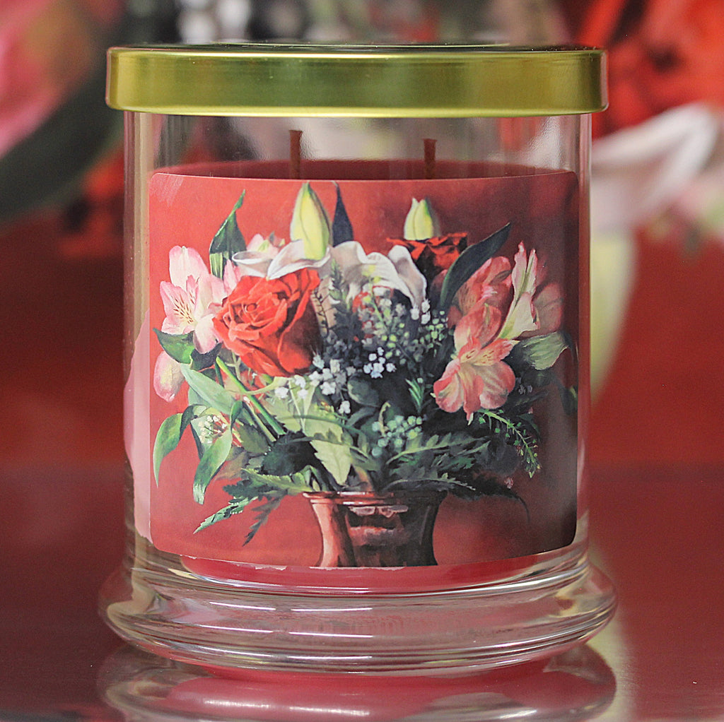 Close up view of an unlit rose vanilla scented candle with original floral artwork on the glass jar.